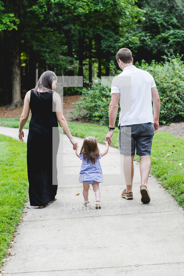 a mother and father walking holding hands with their daughter 