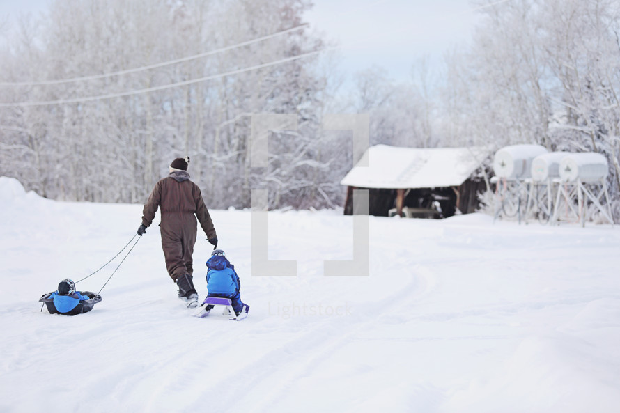 A man pulls two children on sleds through the snow.