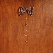A bowtie and buttons lined up on a brown table.