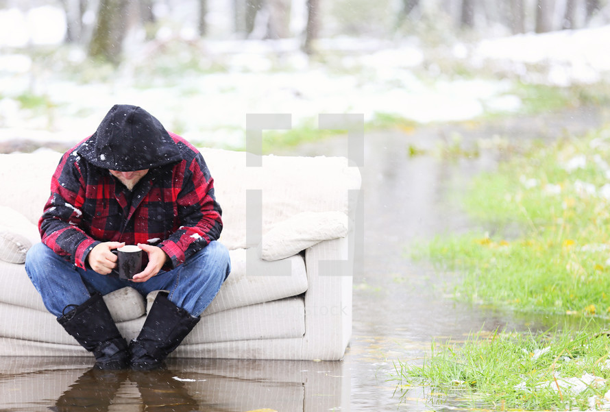 A man sits on a couch that is outside sitting in water.