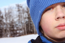 A boy in a blue winter hat outside in the snow.
