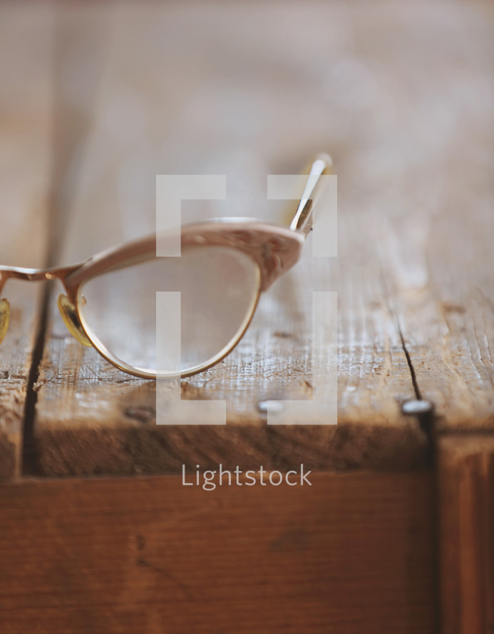 Eye glasses on a rugged wooden table.