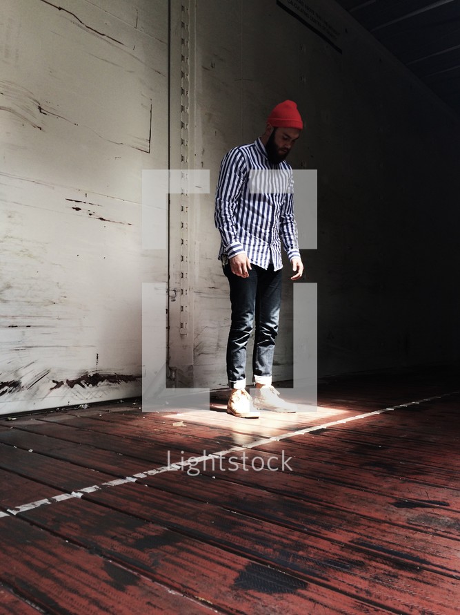 man standing in a spot of sunlight in an empty warehouse 