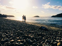 A couple walking along a beach covered  with black rocks