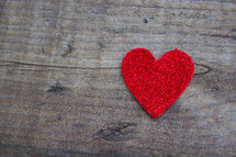 A single red heart on a rugged wooden board.