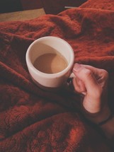 hand holding a mug of hot cocoa over a warm blanket 