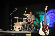 Drummer on stage with a guitar.