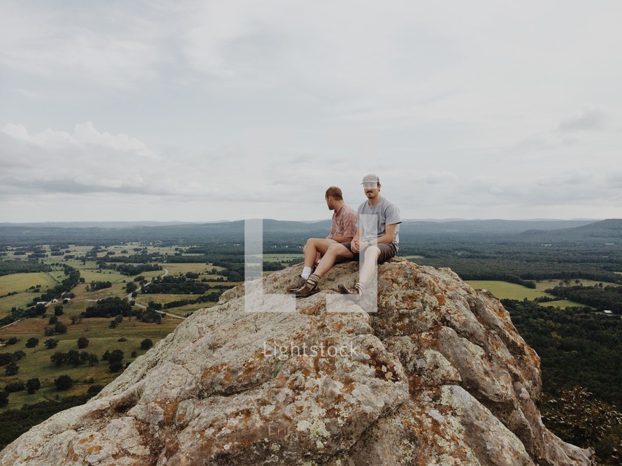 two men sitting on a rock peak