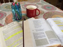 jar of pens, open Bible, journal, and coffee mug on a table 