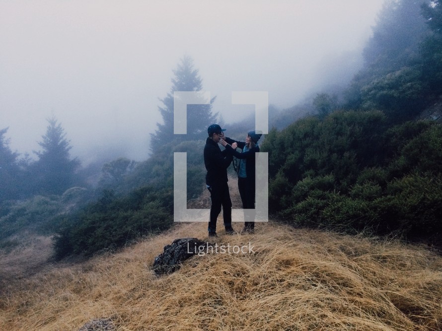 man and woman standing on a foggy mountain top 