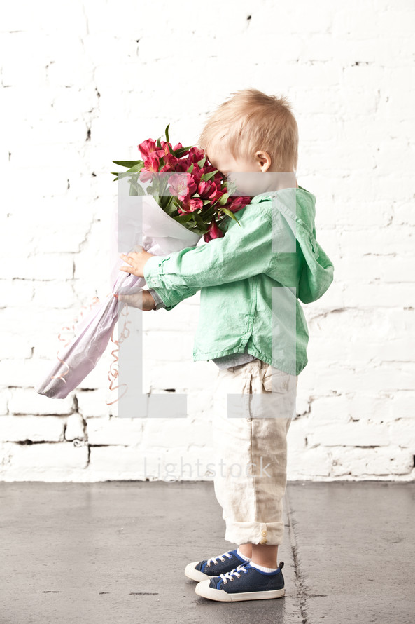 little boy holding a smelling a bouquet of flowers