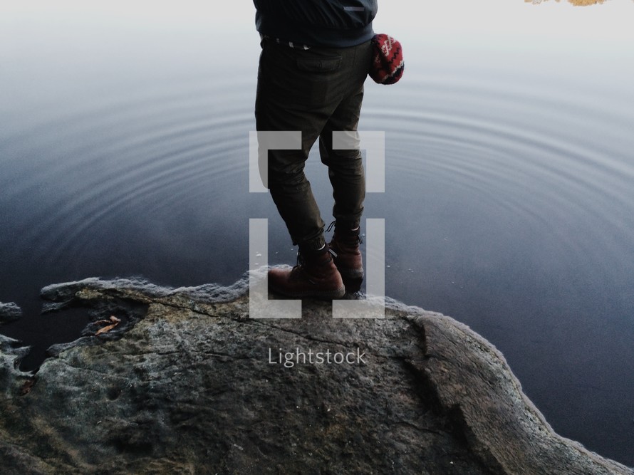 man standing on a rock at the edge of a lake 