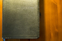 A black leather Bible on a wooden table.
