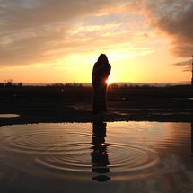Silhouette of person at sunset with reflection in the water.
