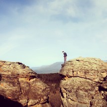 Man standing on mountain top, looking down in the valley between two boulders.