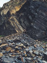 man sitting on a rock pile near a cliff 