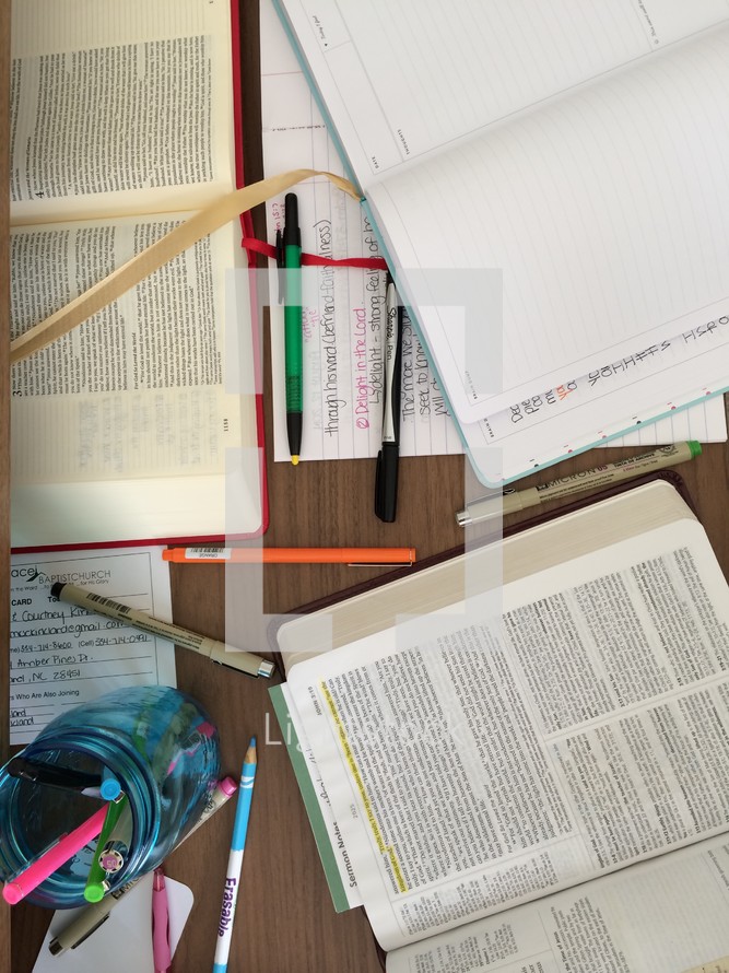 Bibles, pens, journals, and highlighters scattered on a table 