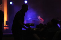 Silhouette of a man passing metal trays to the audience at a concert.