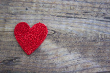 A single red heart on a rugged wood board.