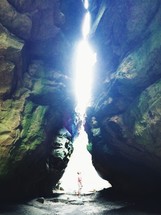 Person looking at the light shining above in the crevasse of two cave boulders.