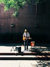 man in a cowboy hat playing music on a street corner 