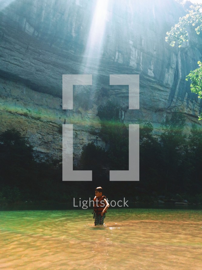 ray of sunlight on a boy with a lifejacket in a river 