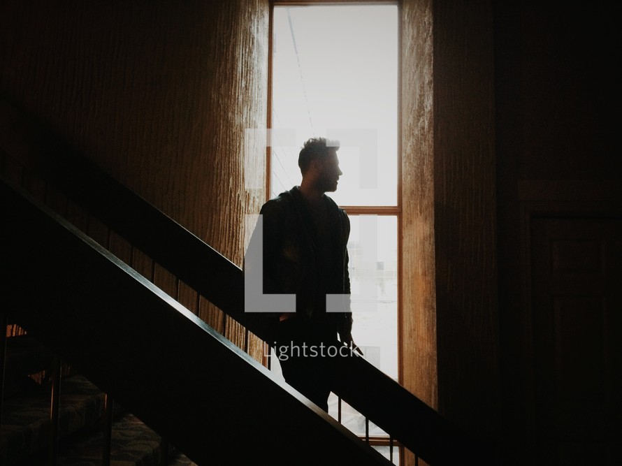 man walking down stairs and looking out a window 
