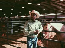 cattle rancher standing near a horse in a stable 