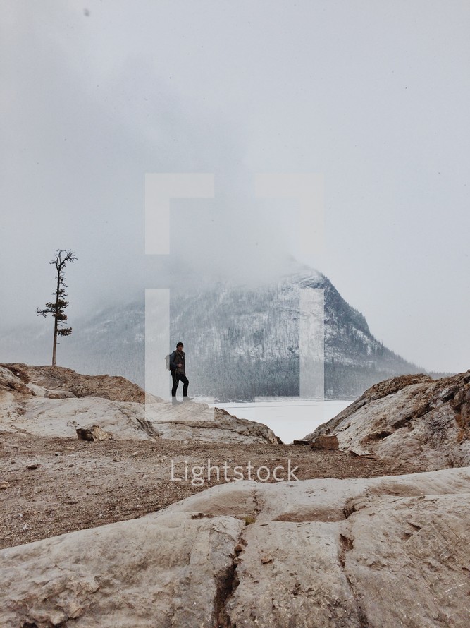 Man standing on a rock looking at a snow-covered mountain.