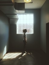 Girl standing alone in front of a window in an empty room.