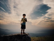 a boy child standing on the edge of a cliff 