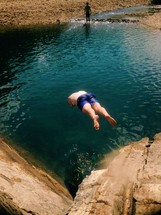 man diving off a cliff into a water hole 