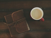 A cup of coffee and a leather journal on a wooden table.