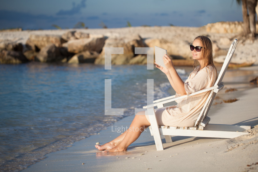 Woman with pad relaxing in chaise-lounge on the beach