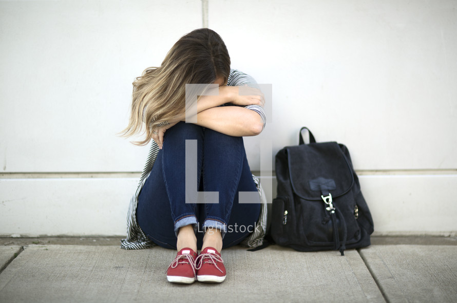 sad girl sitting next to a book bag 