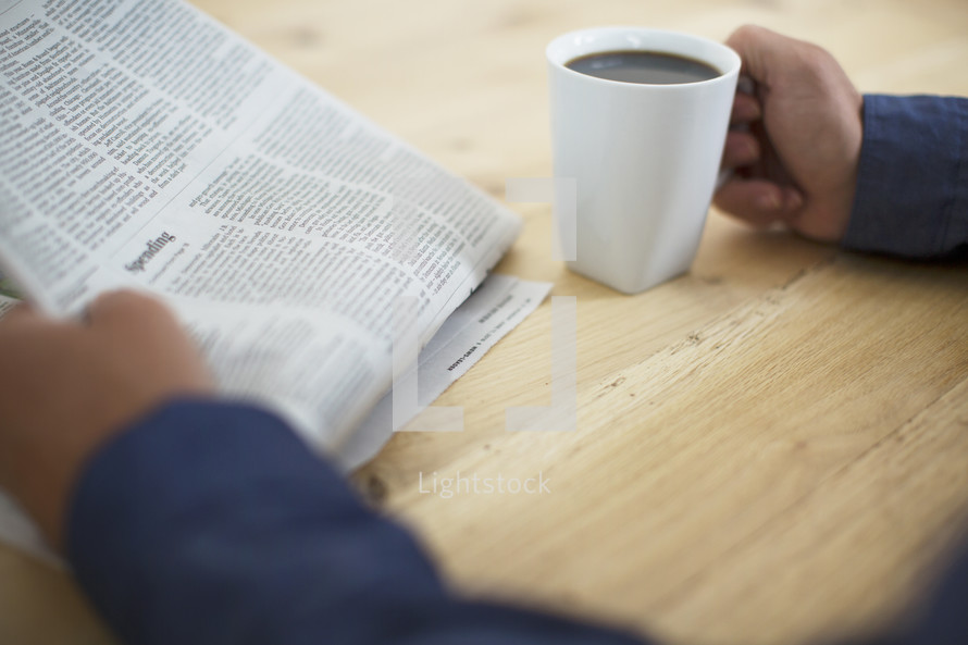 a man reading a newspaper and drinking coffee 