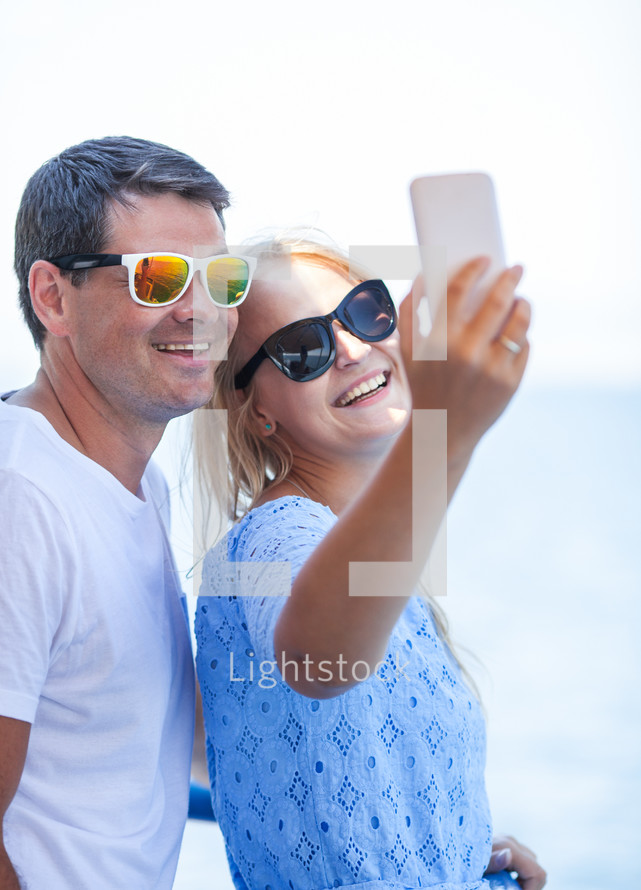 Cheerful couple in sunglasses taking mobile selfie