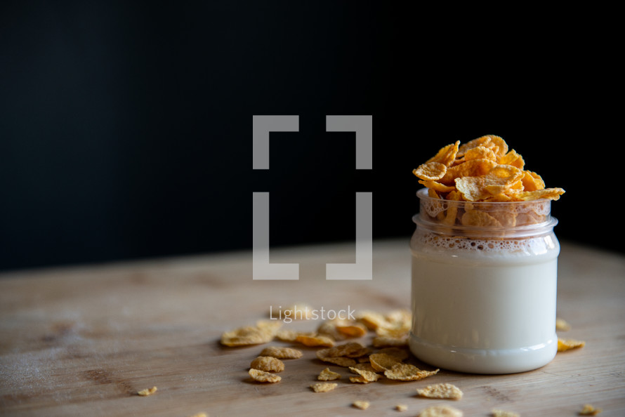 jar of yogurt with cornflakes stands on a wooden board and black background