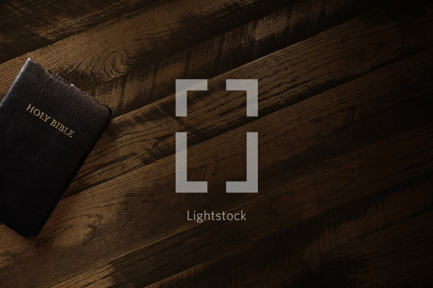 A leather bound Bible laying on an old wooden table in a dark room. 