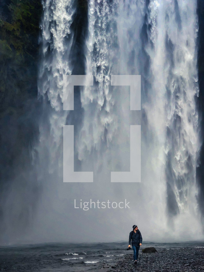 a man walking in front of a waterfall carrying a camera 