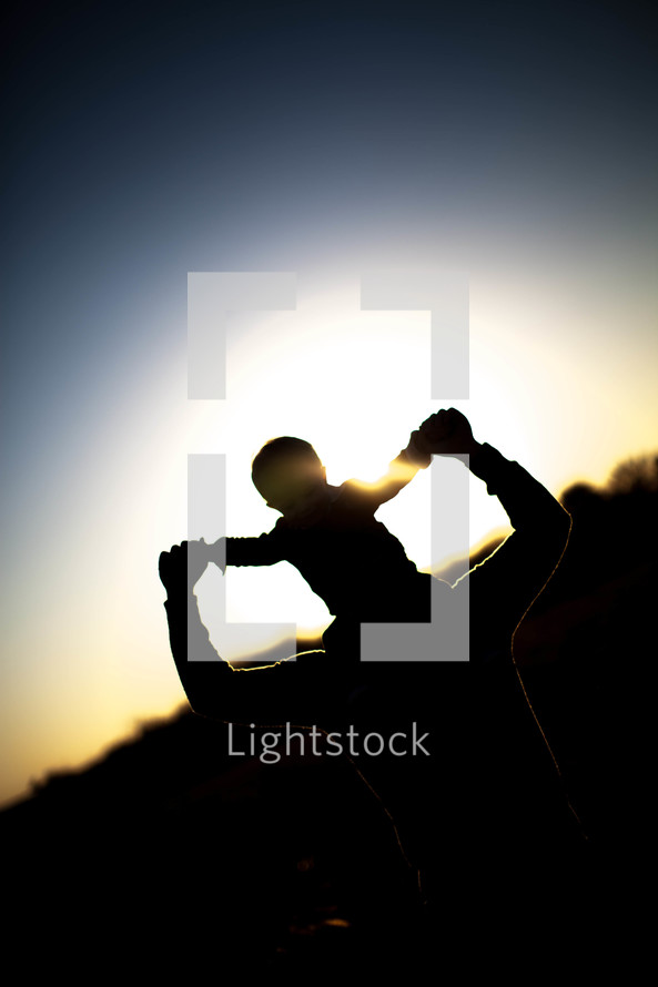 Silhouette of boy riding on man's shoulders at dusk.