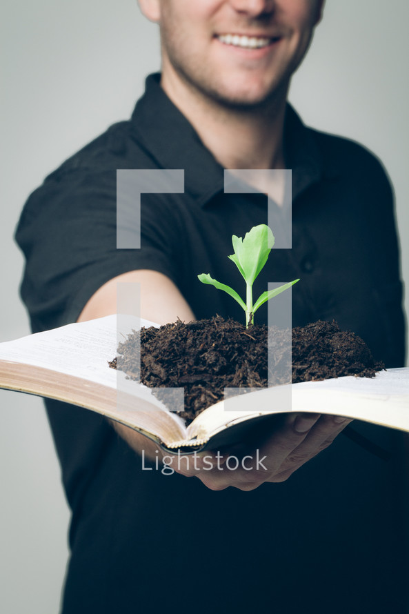 man holding a Bible with soil and a plant growing in its pages