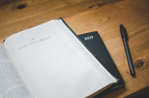 A bible open at the new testaments sits on a 2017 diary on a desk with a pen