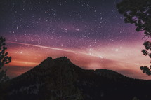 stars in a night sky and silhouette of a mountain peak