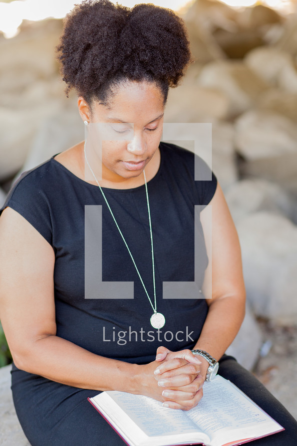 African American woman with praying hands over the pages of a Bible 