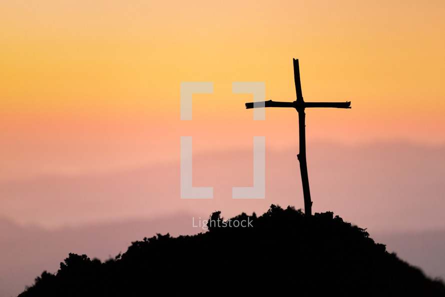 Wooden cross on a hill with a vivid sunset background