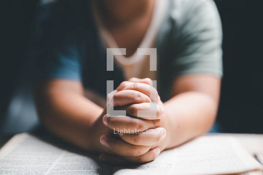 Person's hands clasped in prayer on a Bible