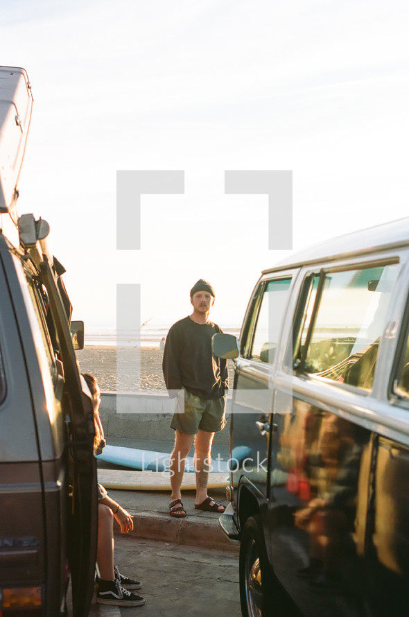 man standing on a beach between VW vans 