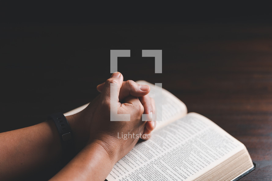 Hands clasped in prayer on Bible