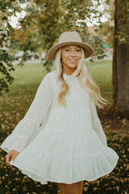 a young woman in a white dress and hat twirling outdoors 